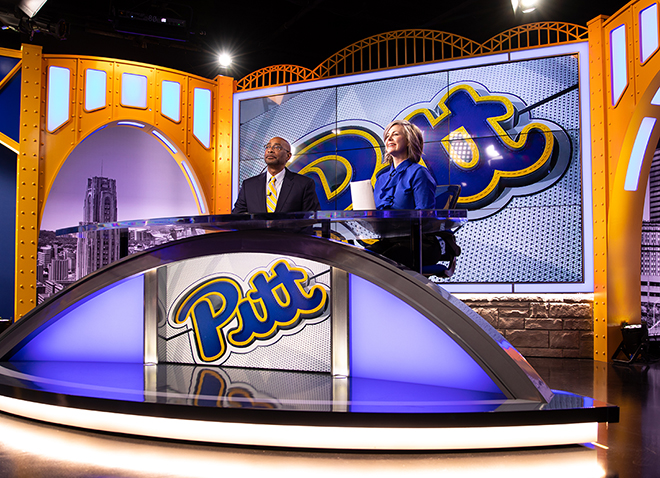 two people at a news anchor desk with Pitt script