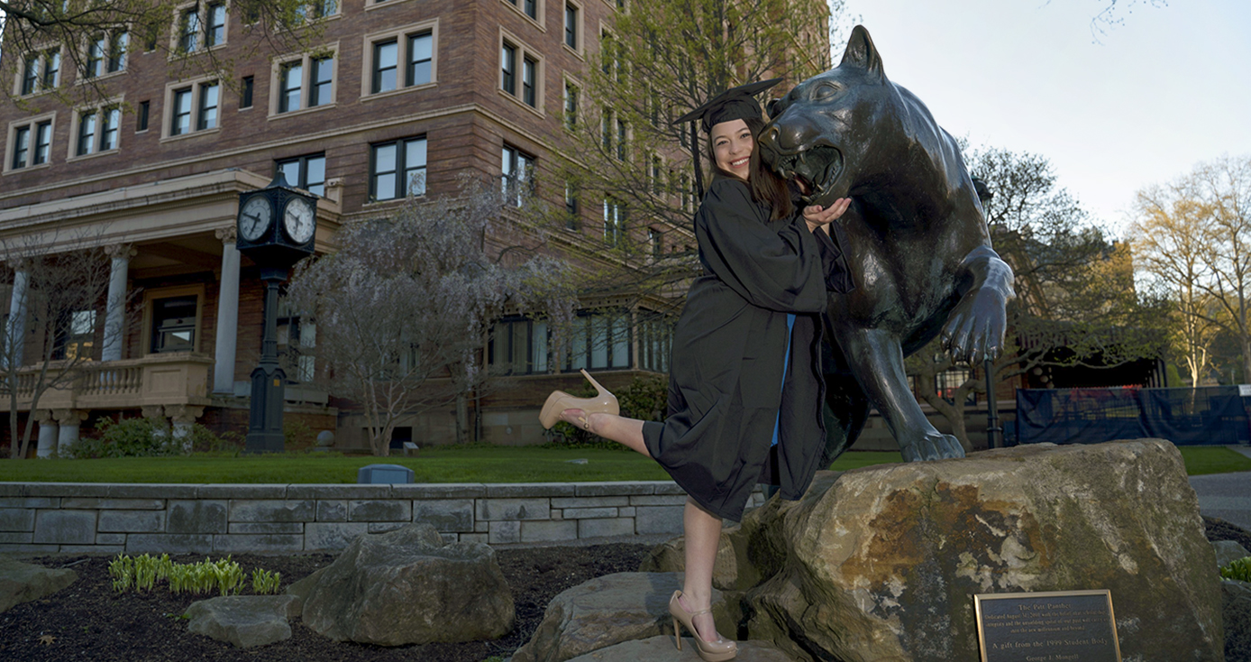 A woman in a black graduation cap and gown posing with a statue of a panther