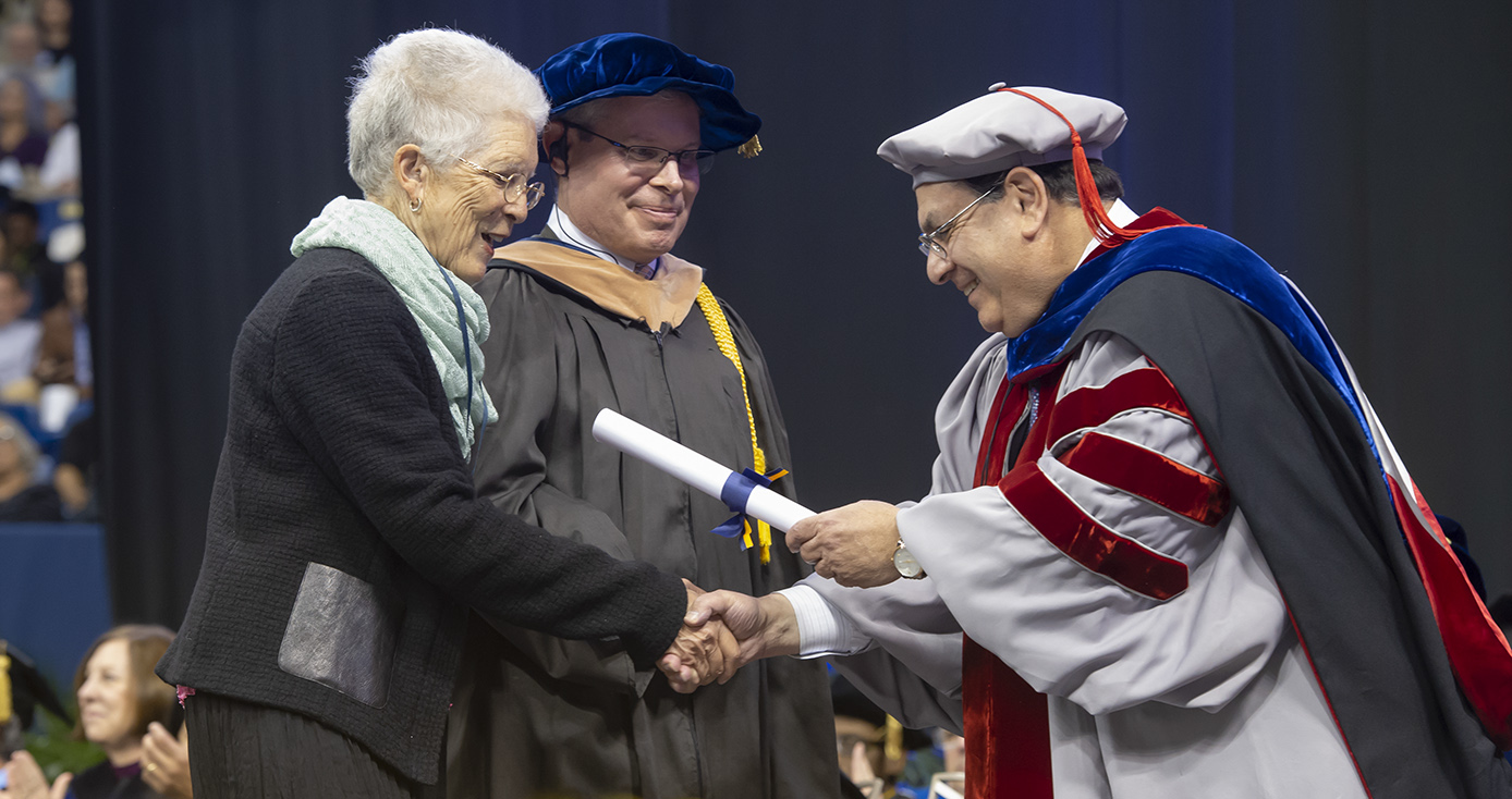Mary Ellen Butler accepting diploma from business school dean, who is dressed in commencement robes, while another man looks on