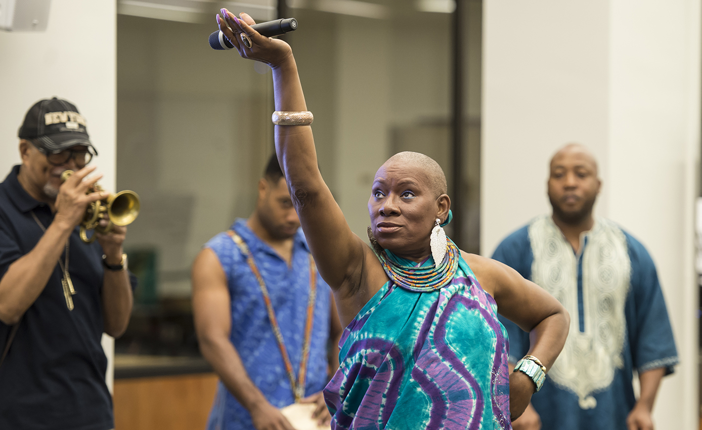 Malaya Rucker performing poetry and dancing with one trumpeter and two drummers in the background