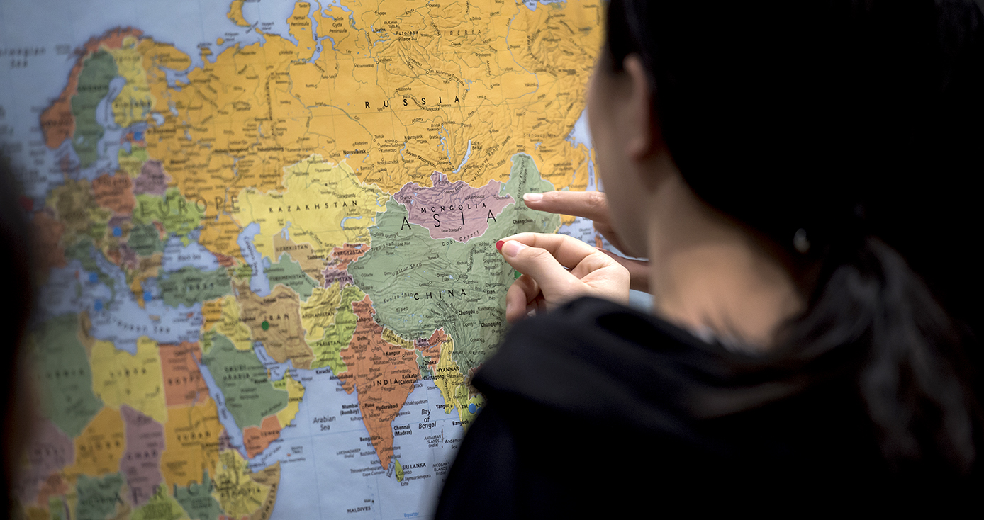 A person in black puts a mark on a map of the world