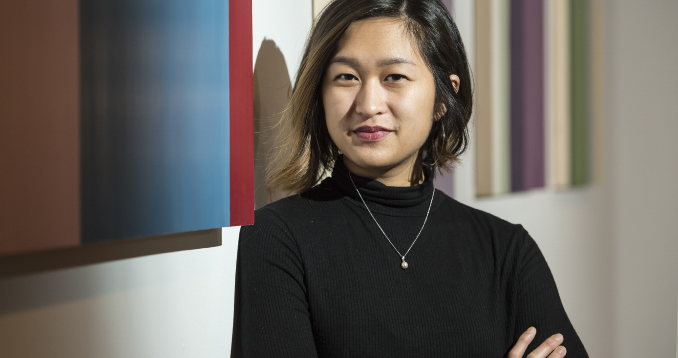 Pearl Galido headshot, wearing black mockneck top and necklace against a background with multi-color stripes