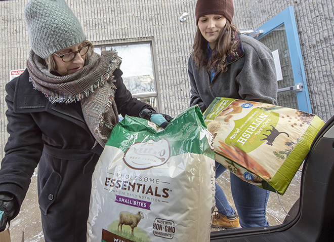 two women unloading bags of pet food from a hatchback trunk