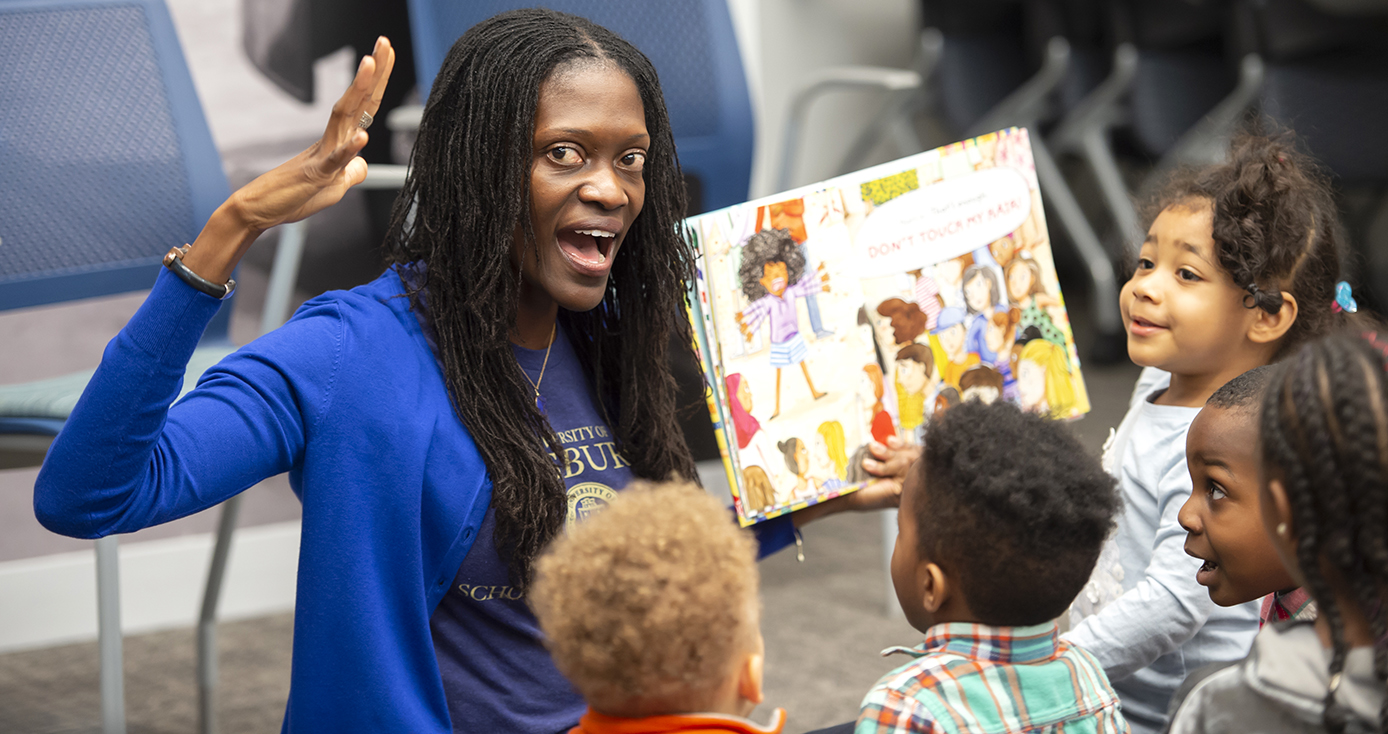 A woman in a blue shirt reading a book to children