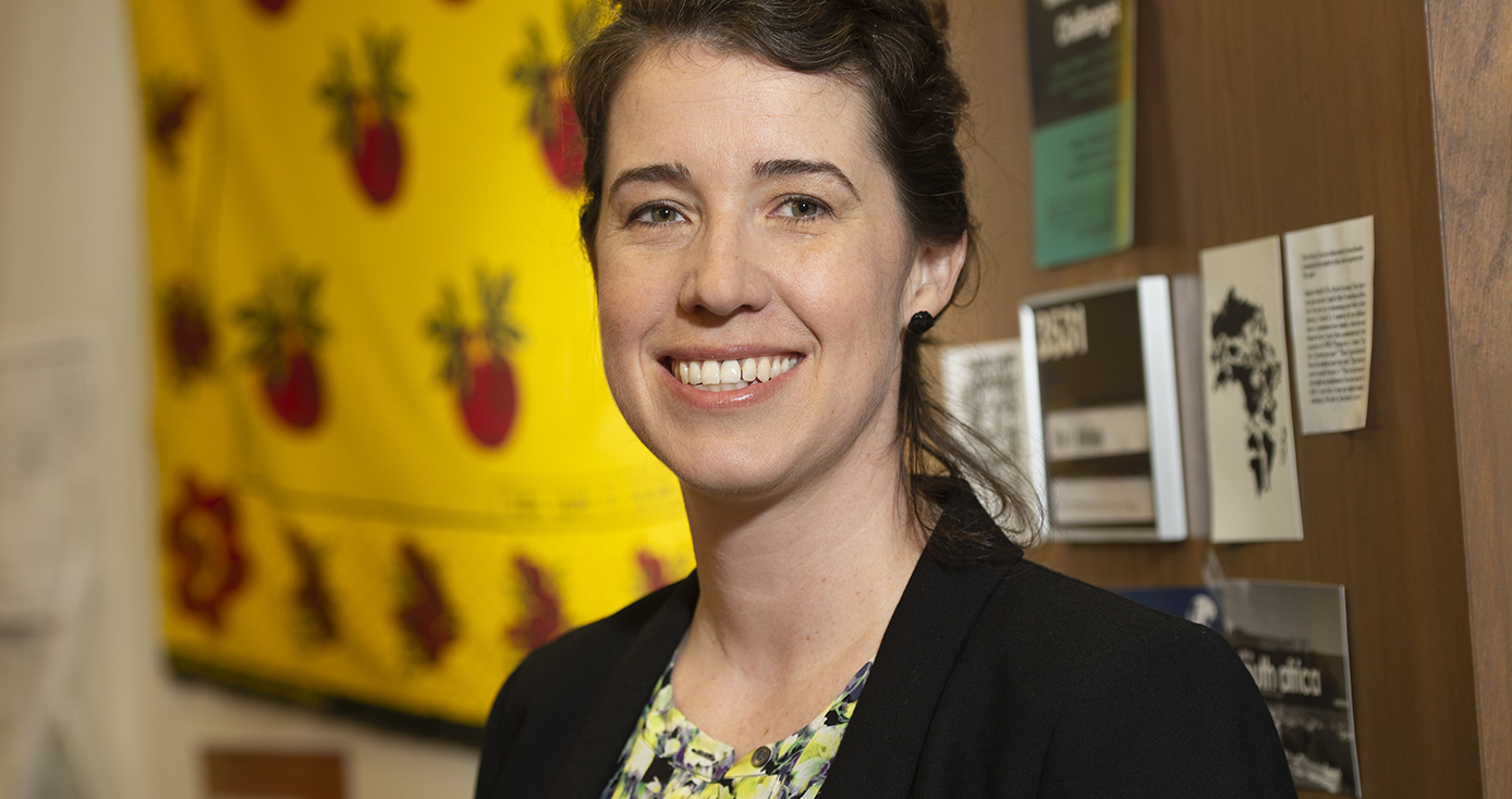 woman in a dark blazer in an office with a bright yellow and red decoration behind her