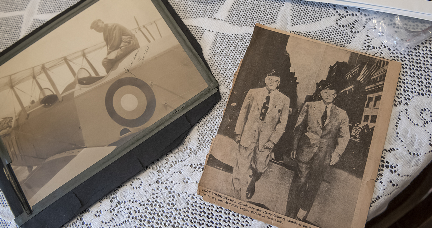an old picture of Colmery in an airplane at left and a clipping from a newspaper at right, all on a lace-covered table