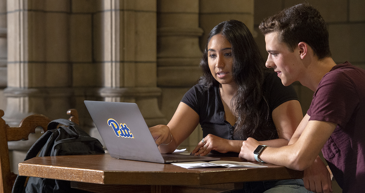 Two people sitting at a table looking at a laptop together