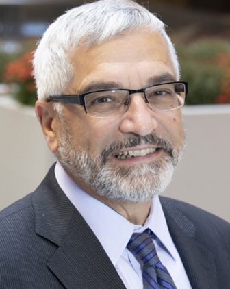 A man with white hair and glasses in a dark blue suit, a light shirt and dark tie