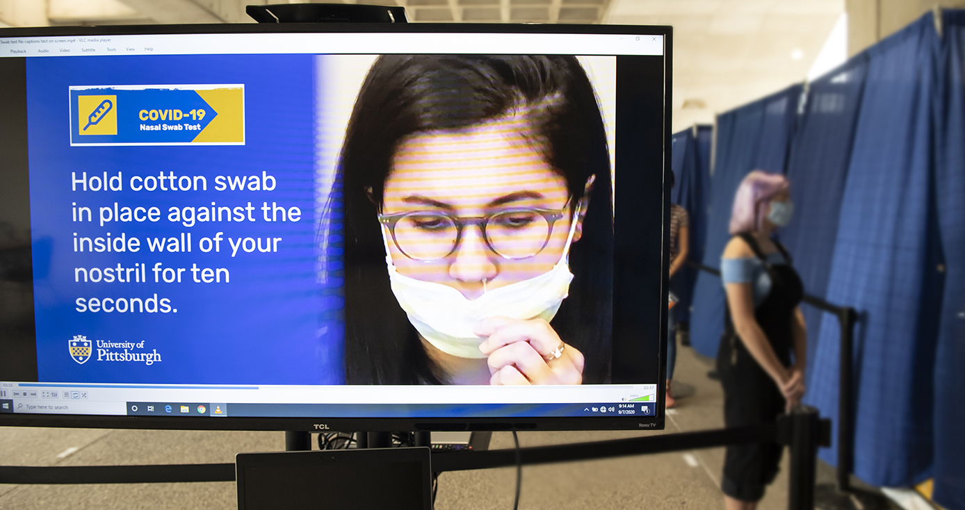 People waiting in line behind a television screen displaying instructions