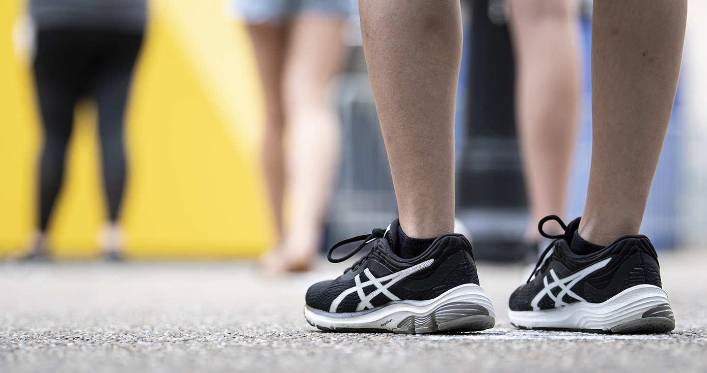 People wait in line. One person wears black sneakers.