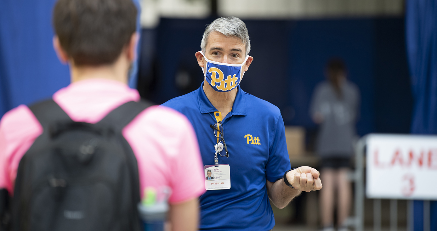 A person in a pink shirt and backpack listens to a person in a blue shirt and face mask