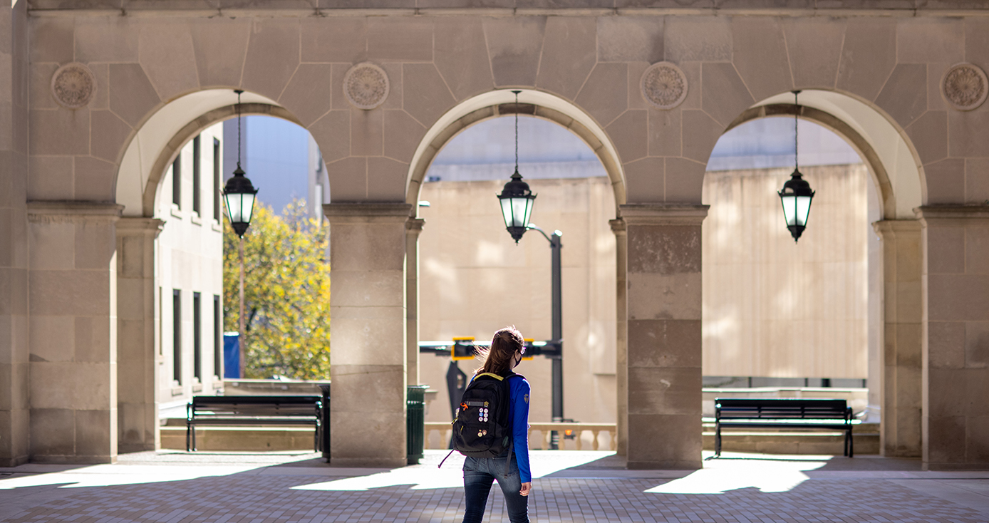A person in a blue jacket and black backpack walks on campus