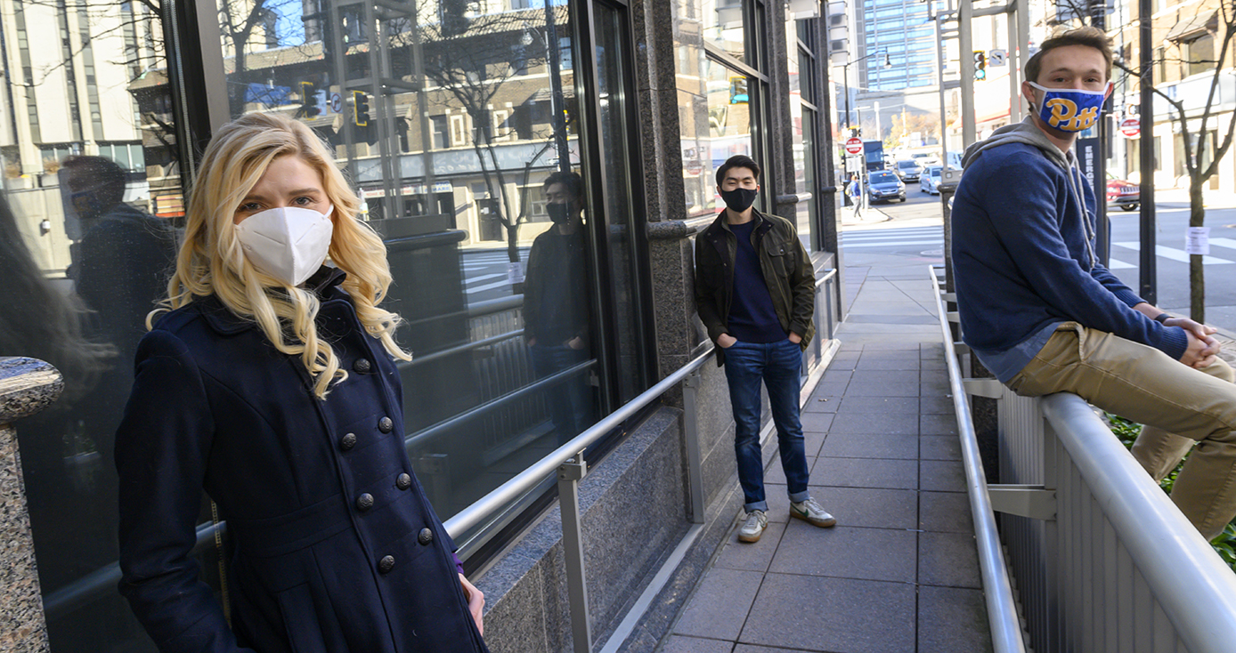 Two people in jackets and face masks on a sidewalk