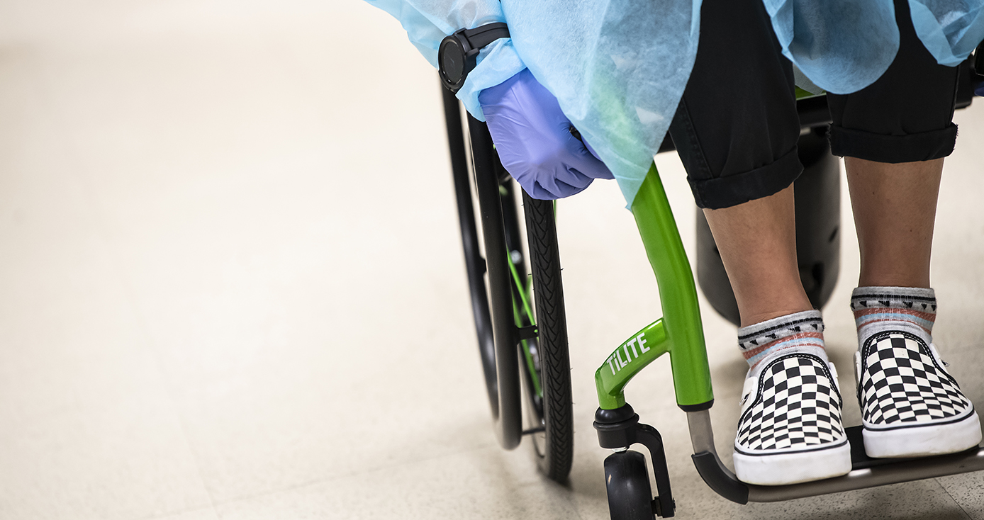 A person in a wheelchair with checkered sneakers, a blue gown and purple gloves