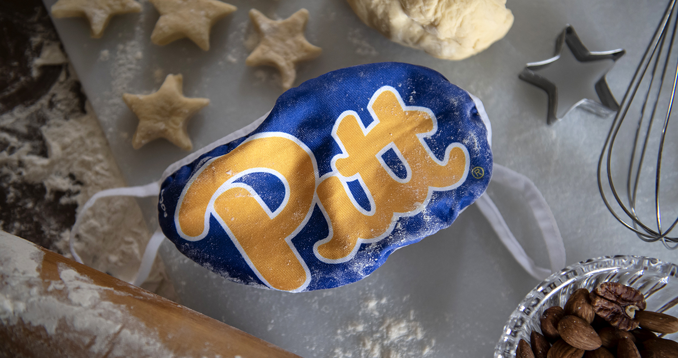 A blue Pitt face mask lying on a table surrounded by cookie dough and cookie cutters