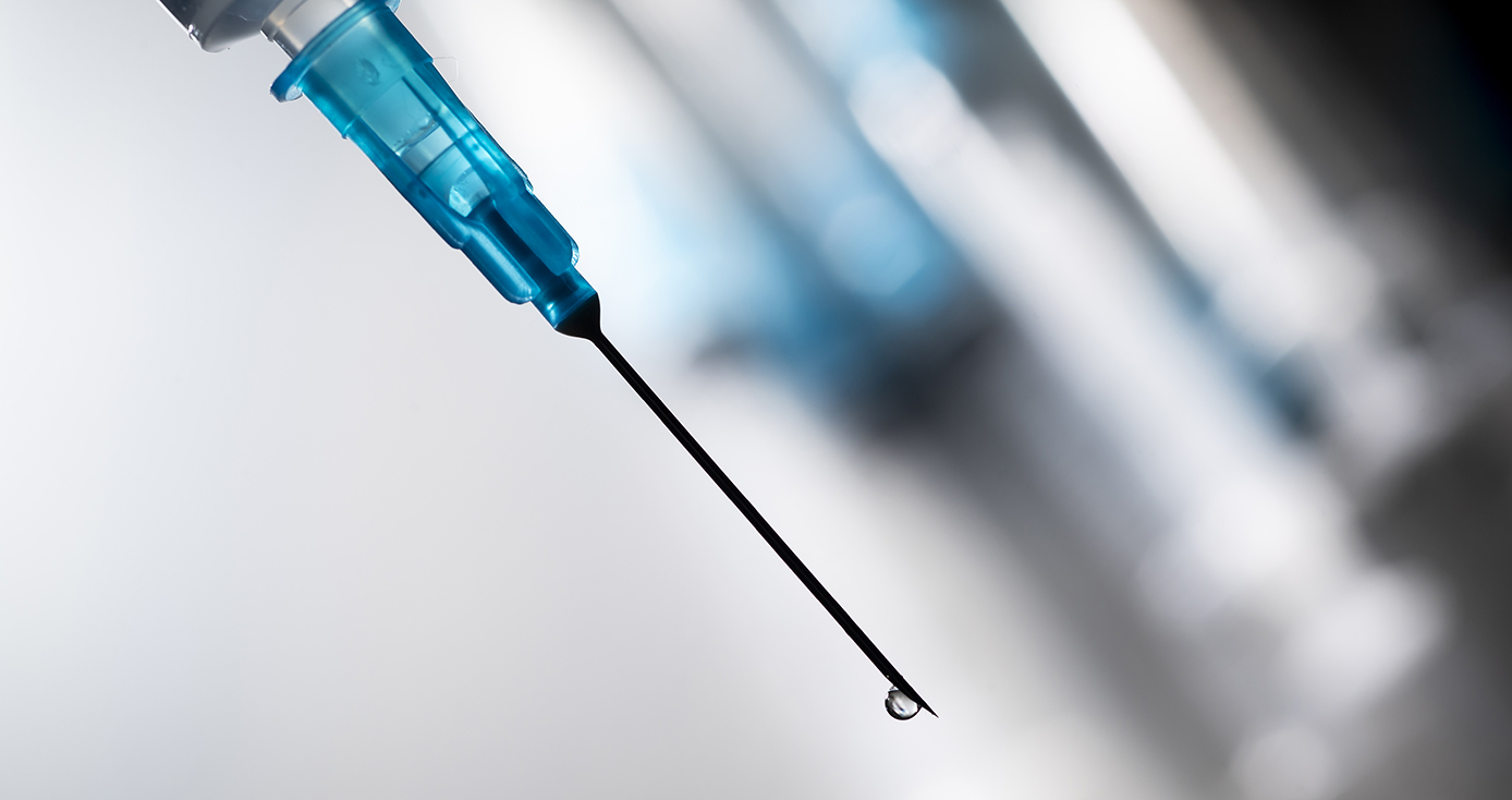 A blue-tipped syringe with a drop of liquid at the end