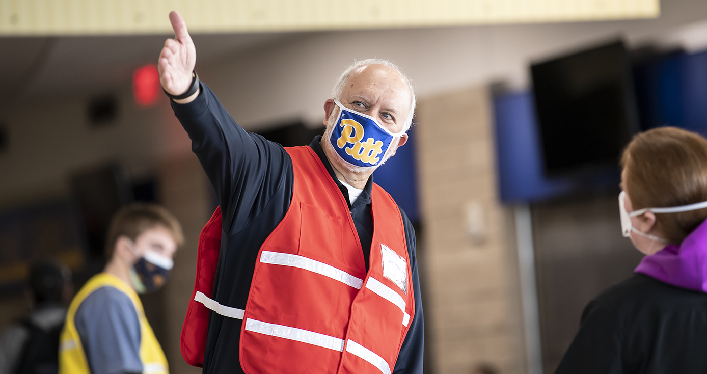 A person in an orange vest and blue face mask points to their right