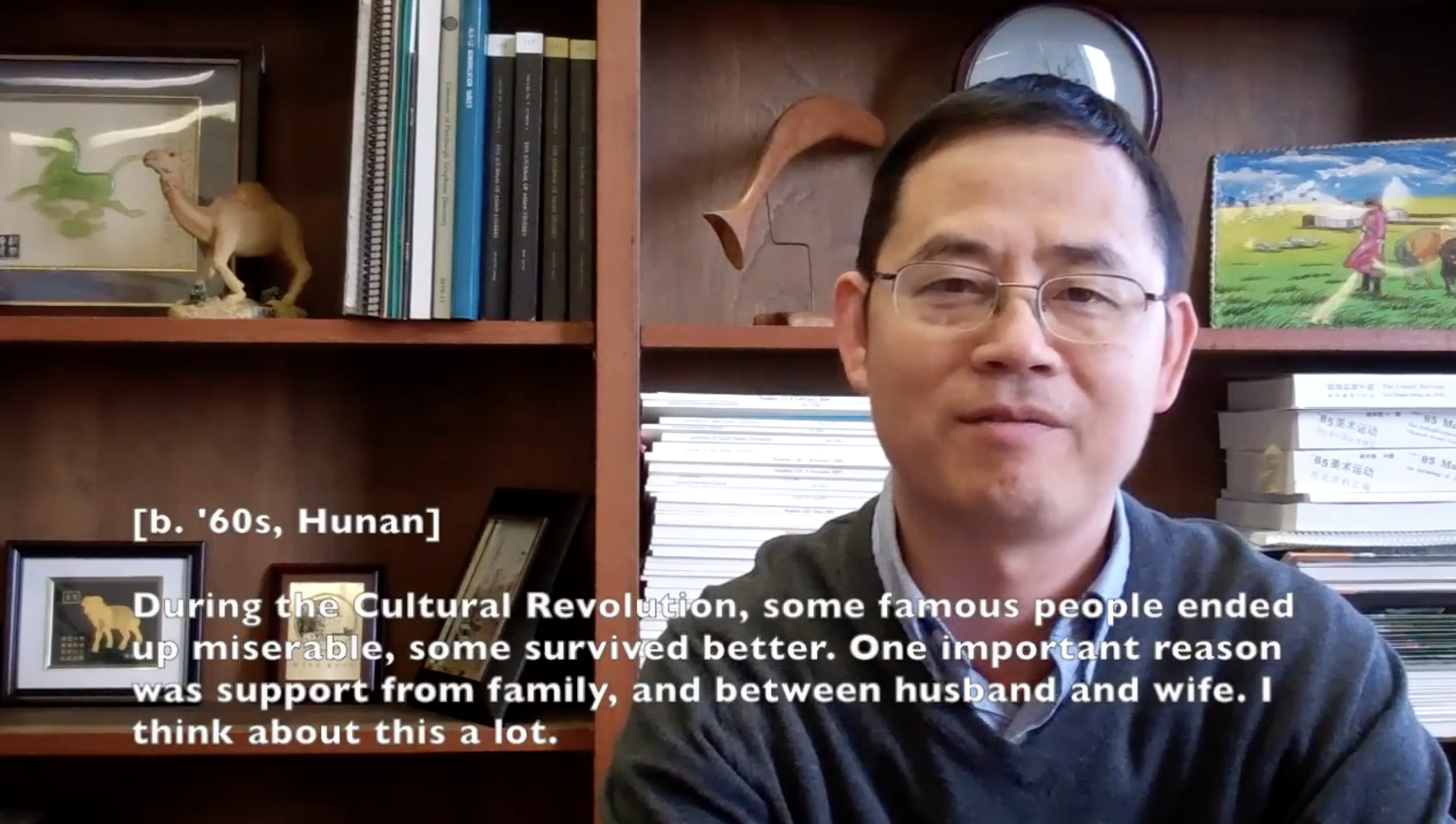 Video still from oral history collection. Man born in 1960s China sitting in front of a bookshel.f