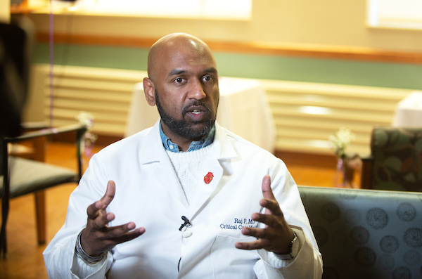 Raj Padmanabhan, wearing white lab coat, seated, gesturing with his hands