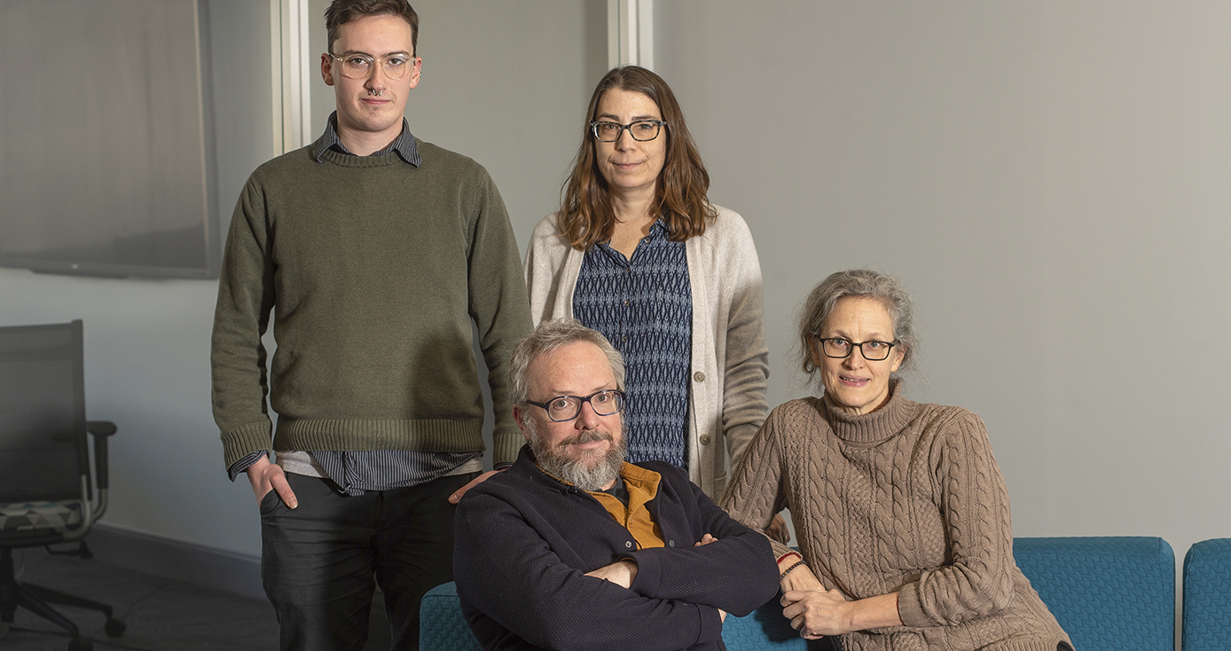 Four researchers wearing business casual clothes pose for the camera on a bright blue sofa. 