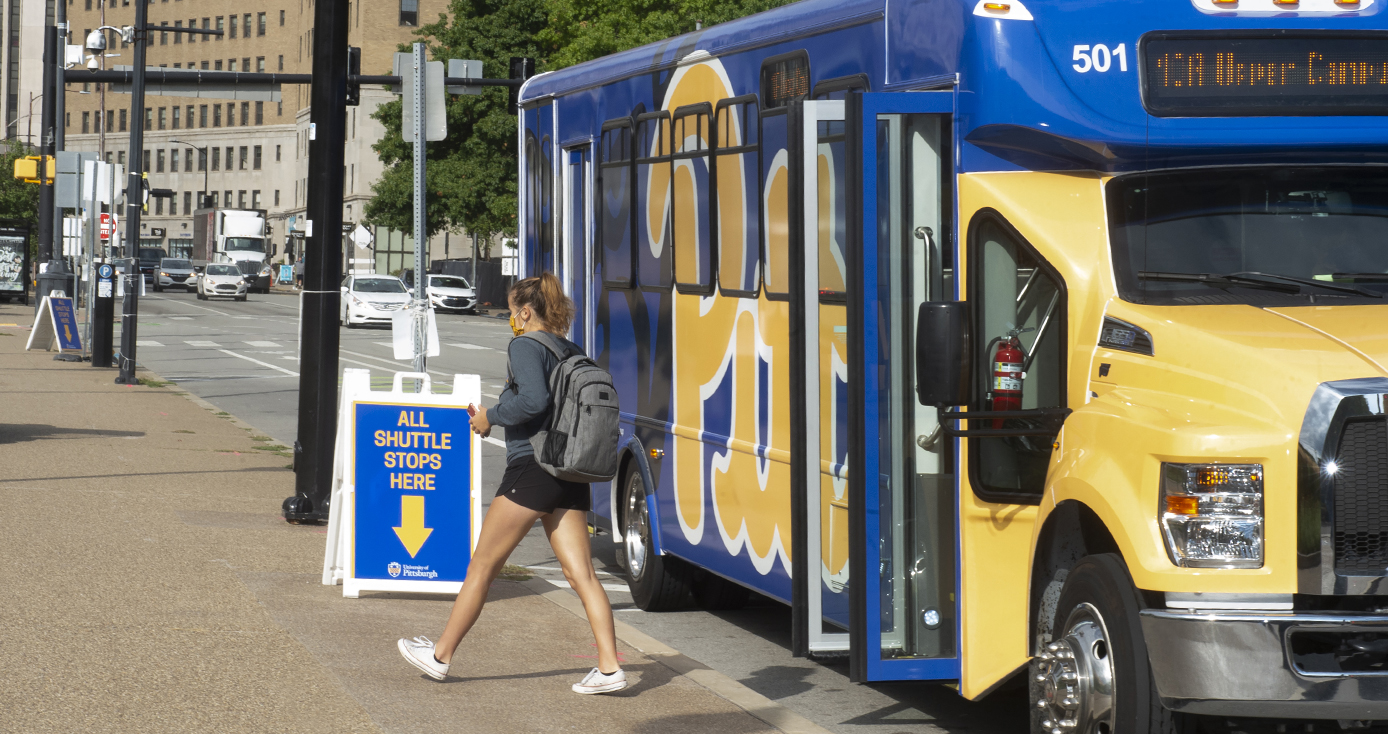 A person with a backpack and face mask disembarks a campus shuttle