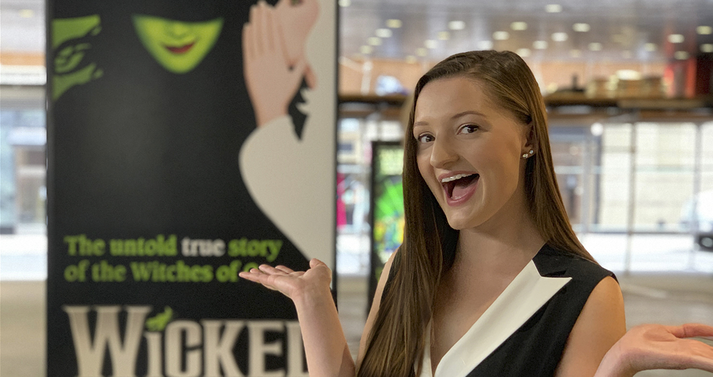 Rachel Noah in front of a banner for the play "Wicked"