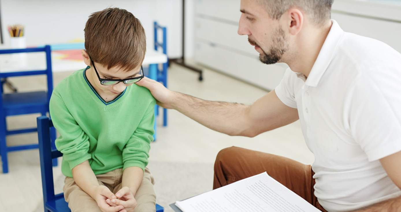 An older man in a white shirt comforts a child in a green shirt 