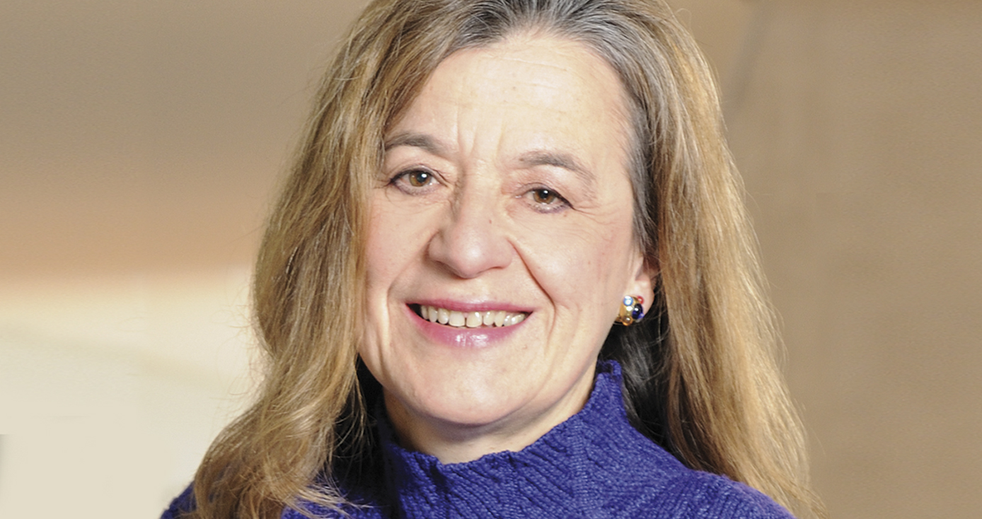 Balazs in front of a tan background, wearing a purple sweater