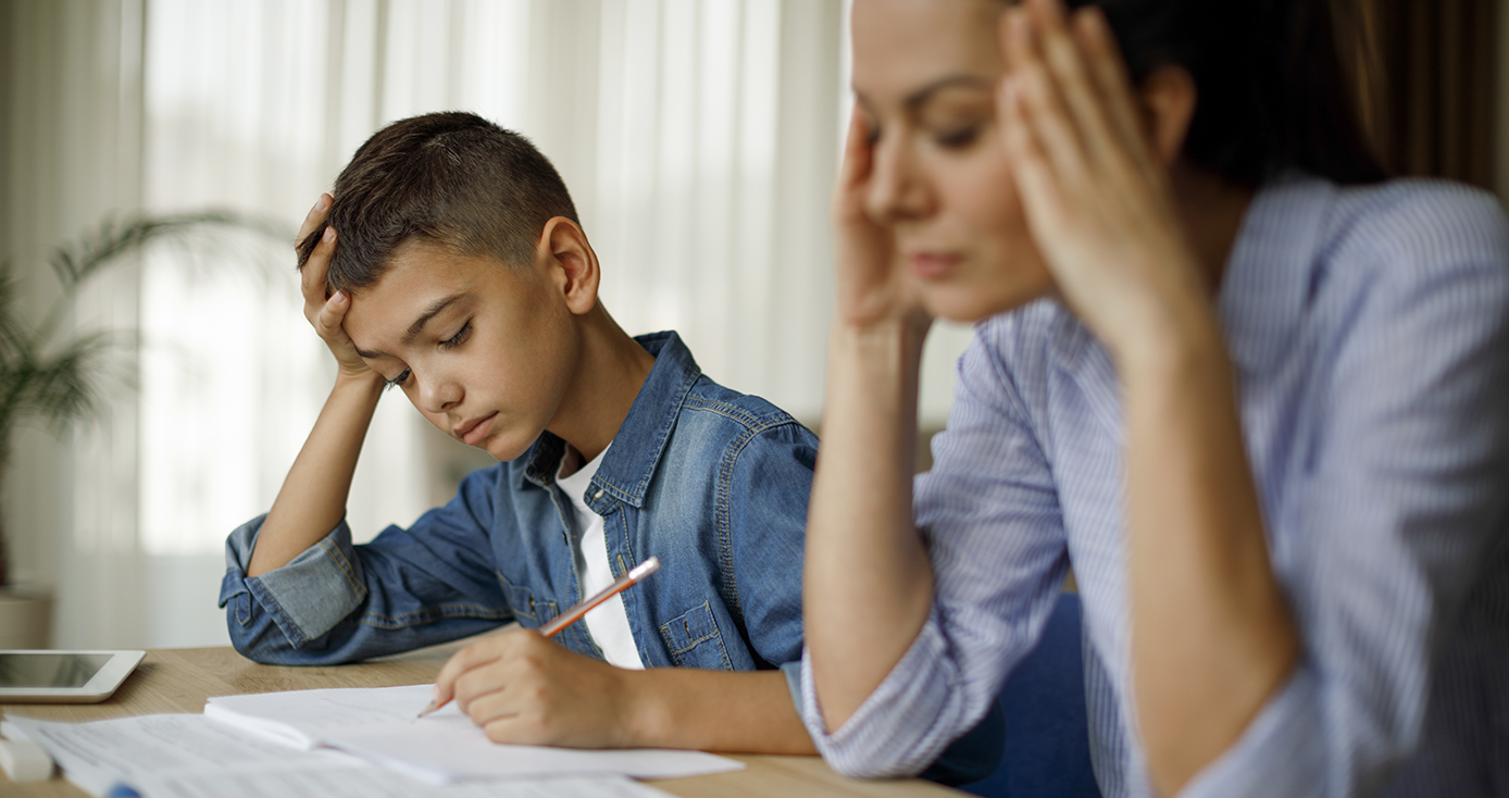 A child and adult sit next to one another at a table, writing on paper.