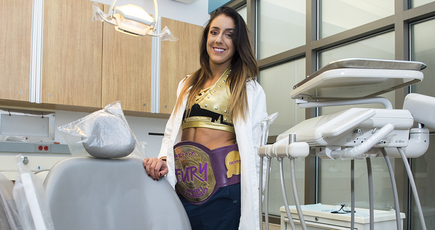 Britt Baker, a woman with long brown hair, wearing a white dentist's coat and a wrestling belt