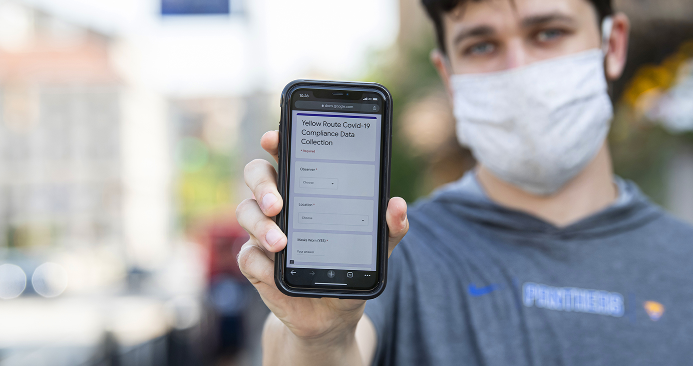 A person in a gray shirt and light face mask holds up a smartphone