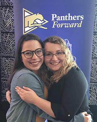 Two people embrace each other in front of a "Panthers Forward" sign