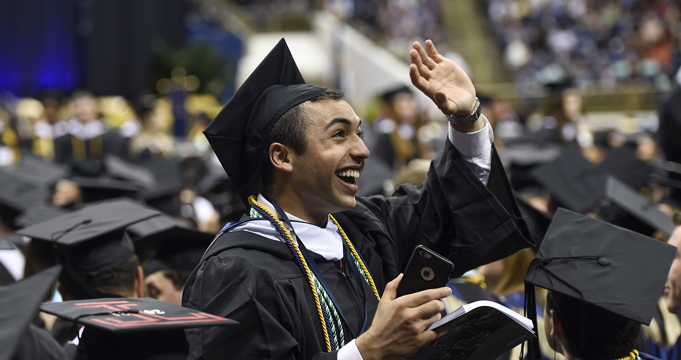 graduate in a cap and gown waving