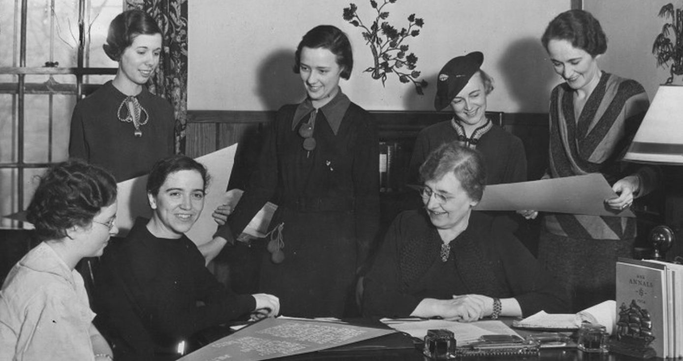 A group of women in a black and white photo sitting and standing together