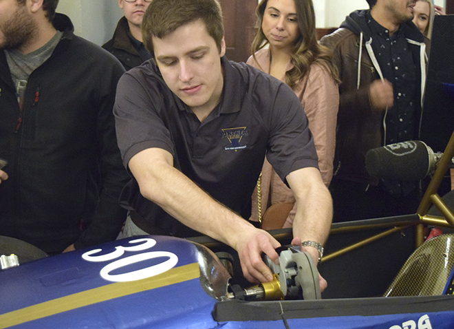 male student working on racecar with a few onlookers in background