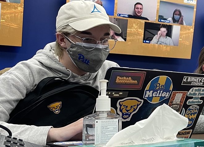 a student in a ballcap and mask staring intently at a computer