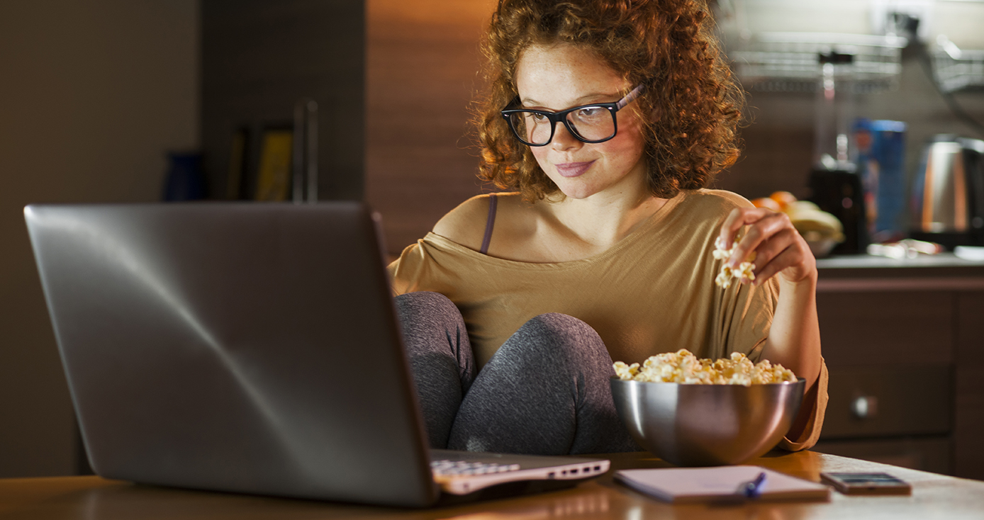 A woman eats popcorn while looking at her laptop