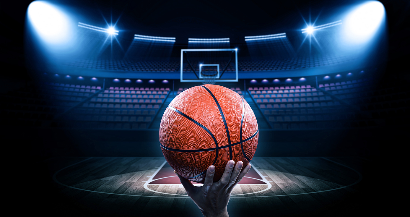 a hand holding a basketball on a spot lighted, empty court