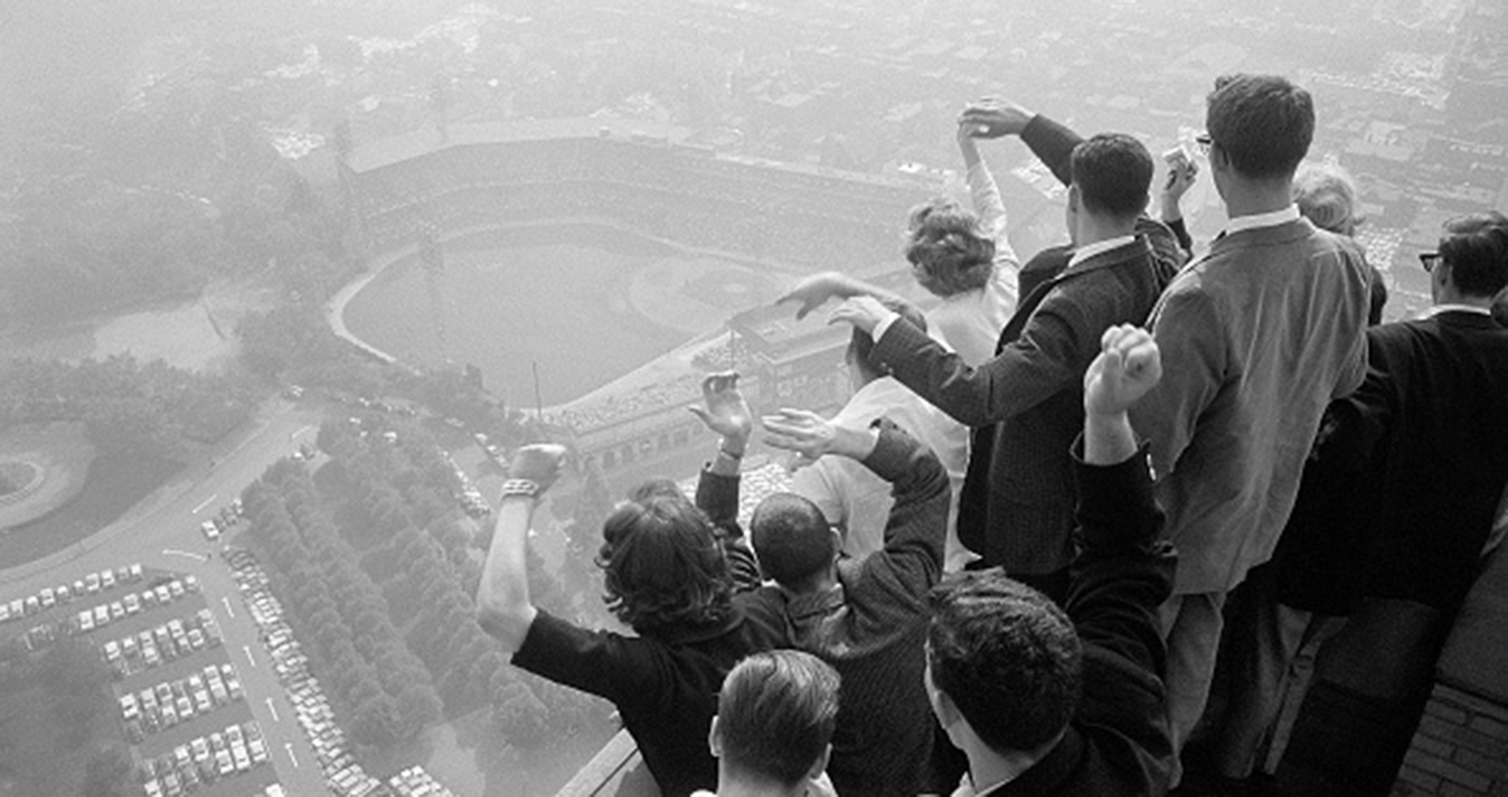 A black and white photo of a crowd of people cheering as they watch a baseball game