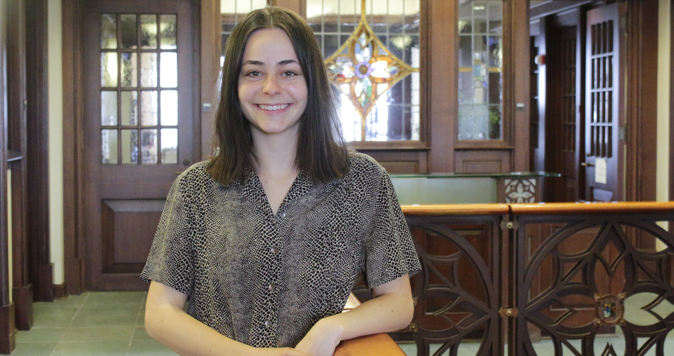 Grace McHale in a gray shirt standing in front of stained glass.