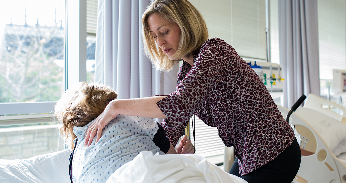 A woman applies pressure to the back of a patient who is clothed in a hospital dress