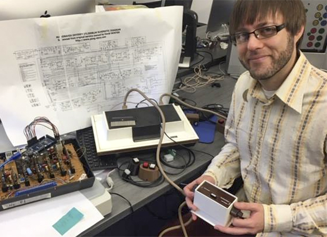 Horton holding a piece of the Odyssey, which sits on a desk in front of a complicated set of plans