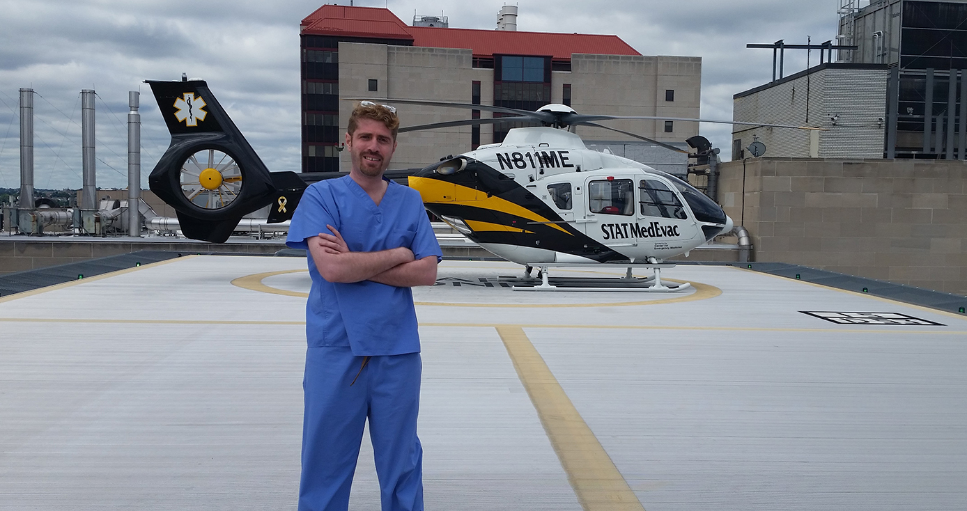 A man in blue scrubs standing by a helicopter