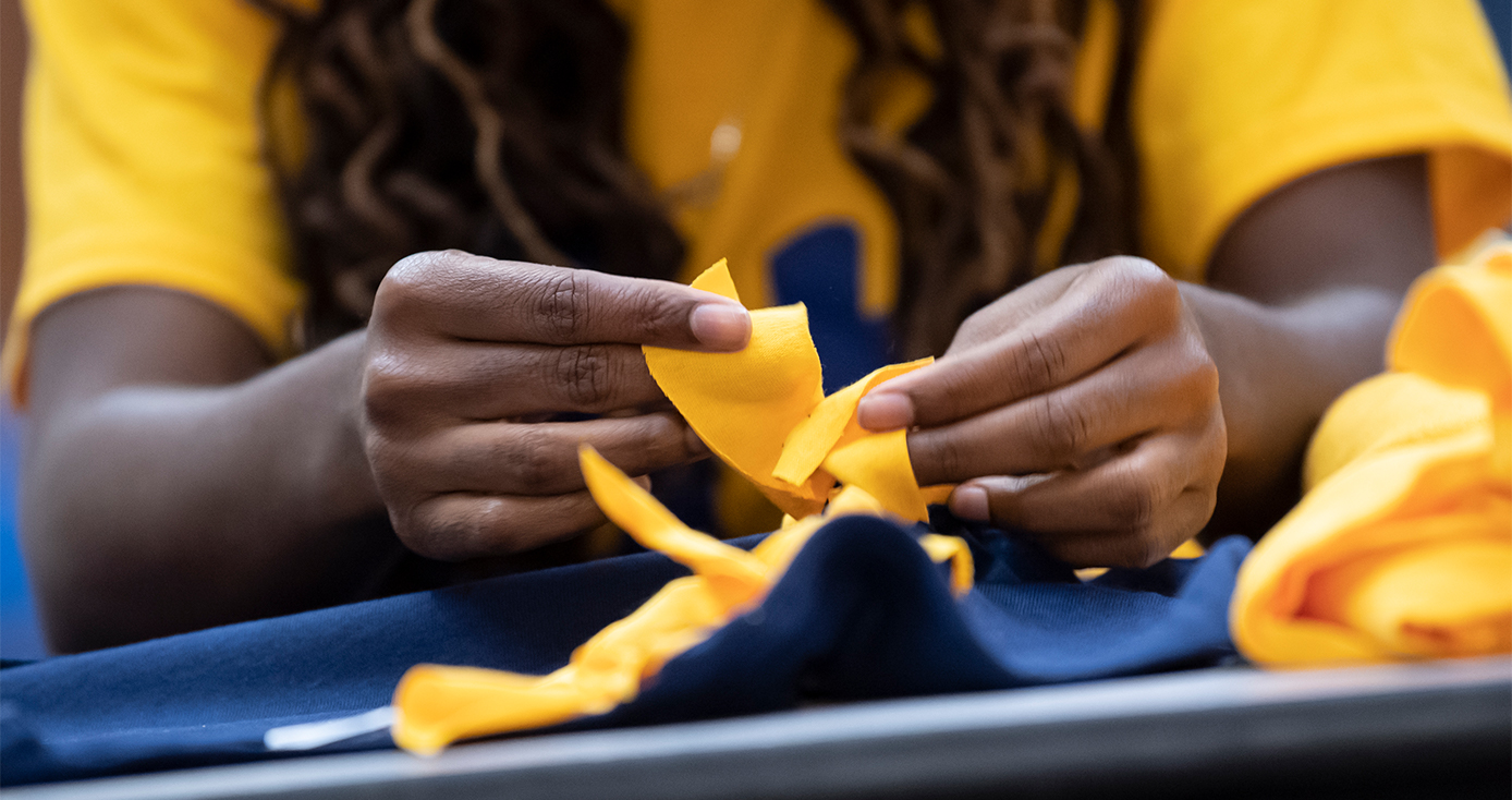 A person in a yellow shirt ties fabric together