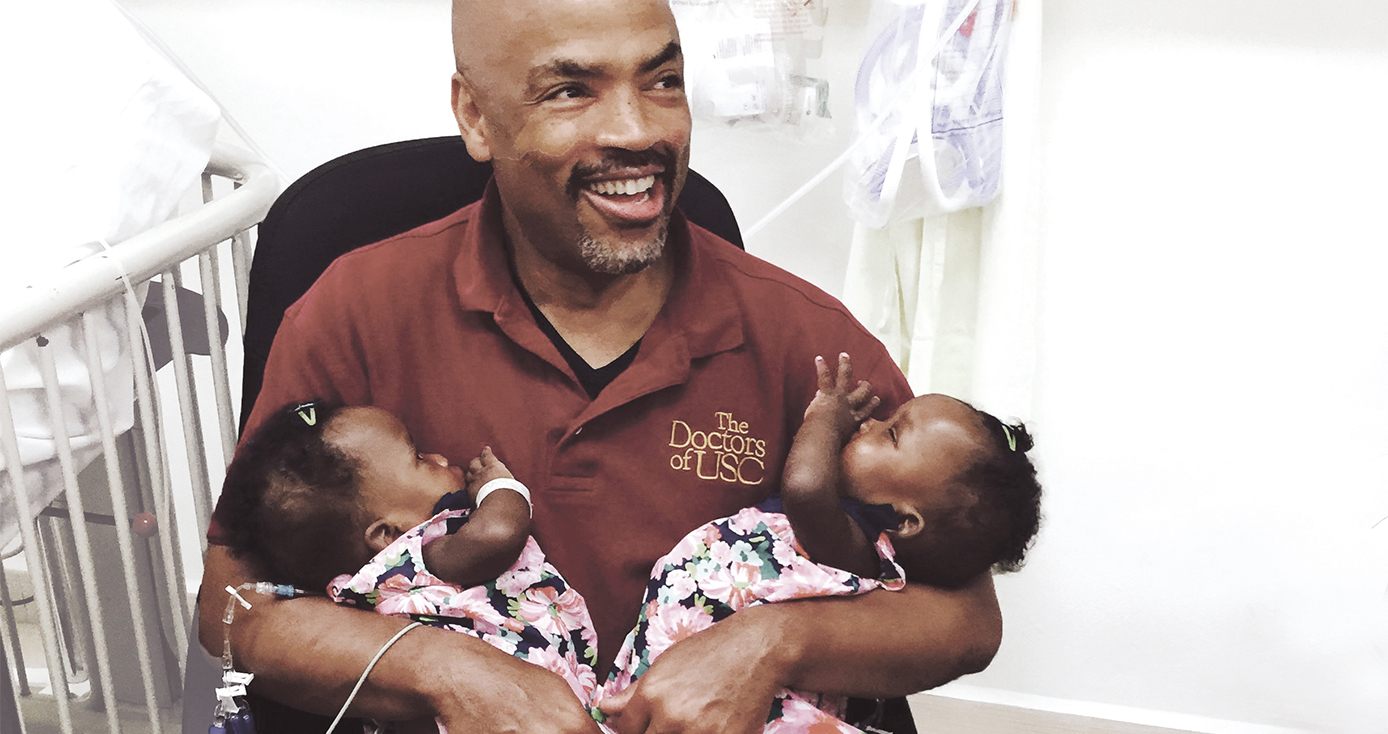 Henri Ford sitting in a red shirt, holding twins in pink dresses