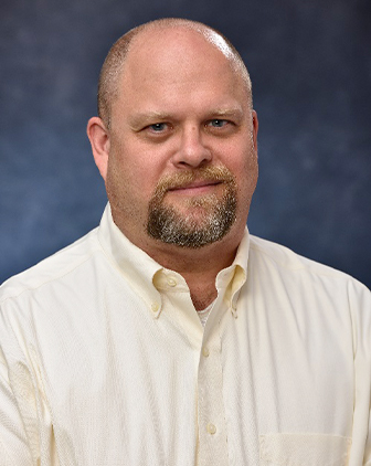 A man in a light yellow dress shirt in front of a gray background