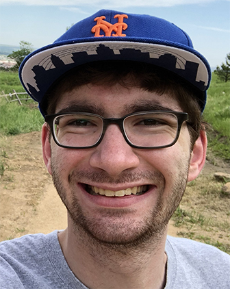 A man in glasses smiles for the camera in a T-shirt and cap