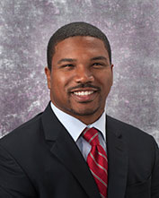 Headshot of Charles Jonassaint in black jacket and red tie with stripes