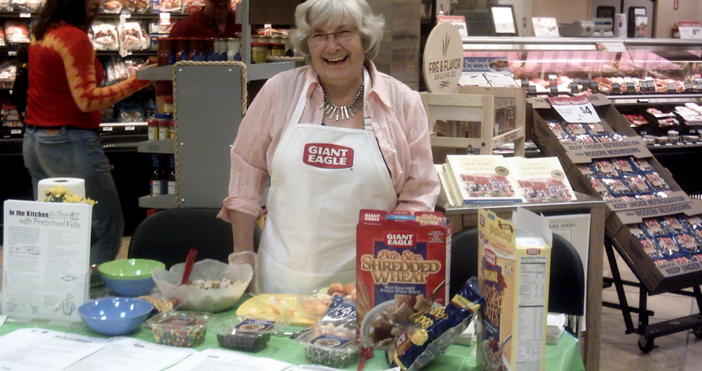 a woman in a Giant Eagle white apron standing behind a table displaying various cereals