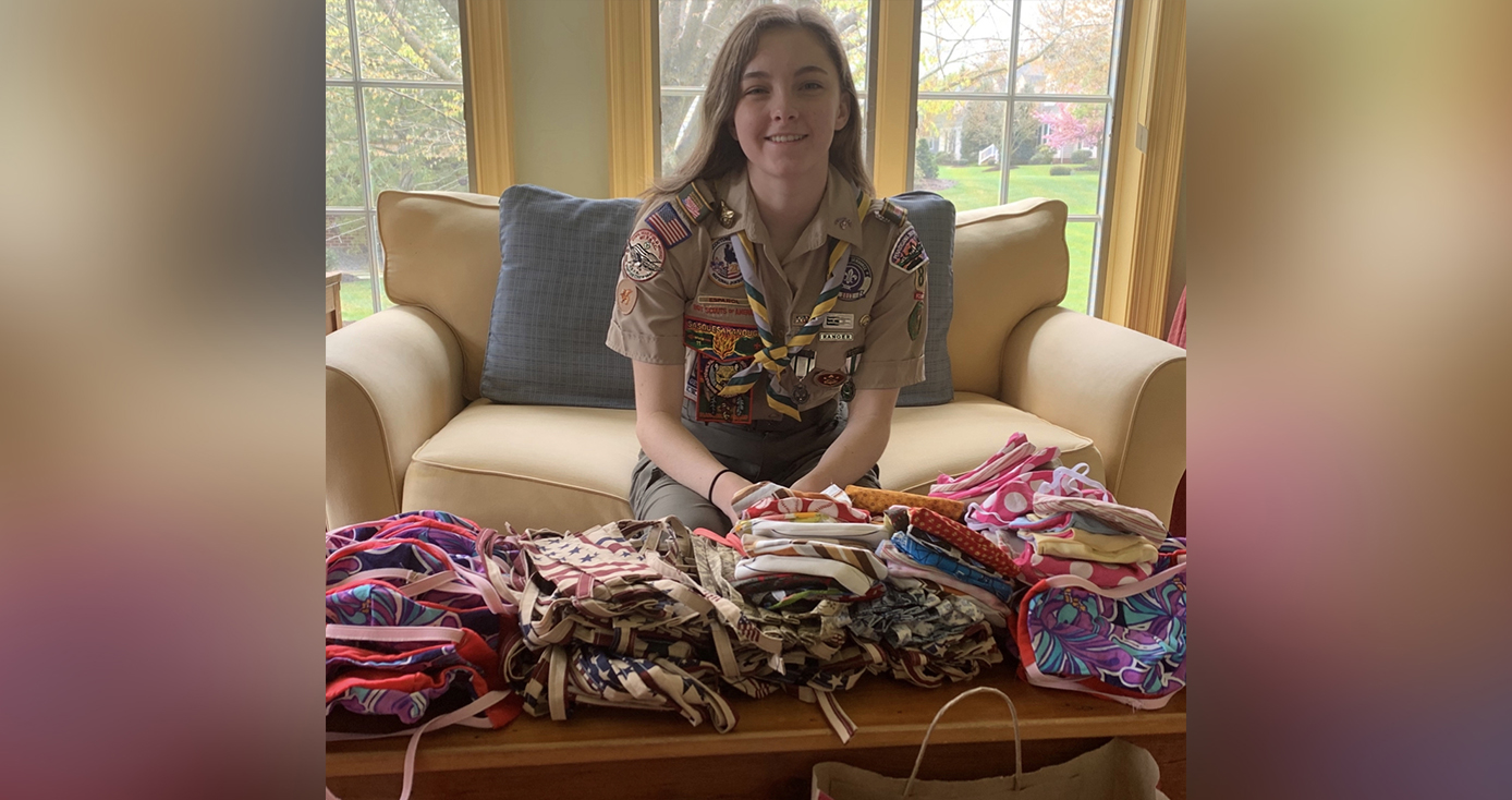 A woman in her Scouts uniform behind a pile of cloth masks